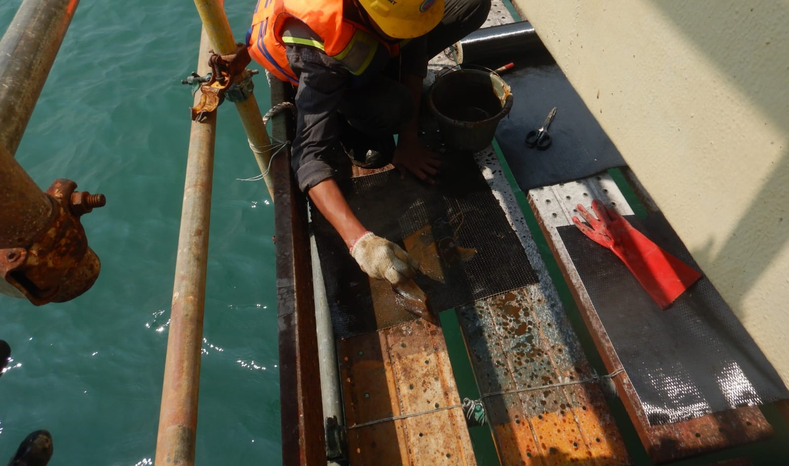 Aplikator mengoleskan resin pada lembaran FRP untuk perkuatan elemen dermaga