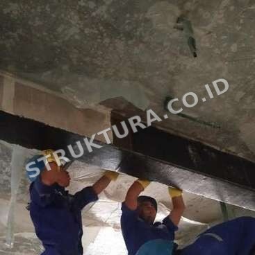 Dua aplikator memasang lembaran FRP pada sisi bawah balok beton
