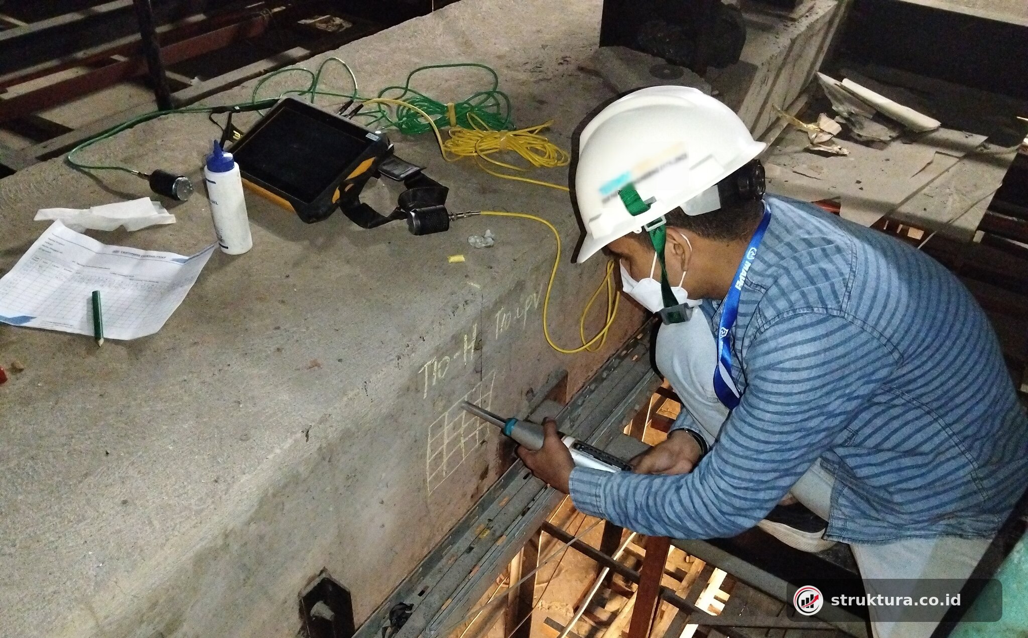 Teknisi melakukan hammer test pada sisi balok beton dengan grid titik uji
