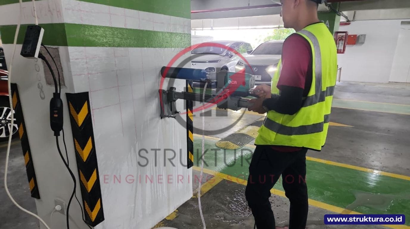 Operator melakukan pengeboran core drill beton pada kolom di area parkir gedung